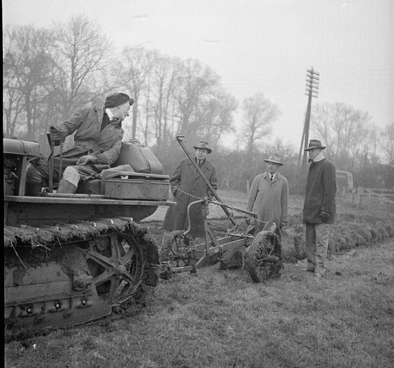 British 'land girl' demonstrates a Chicago-built Lend-Lease tractor to visiting American farmers, somewhere in Buckinghamshire, England [Public domain, IWM/wiki]