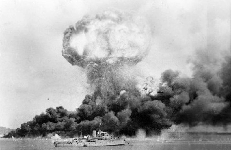 Oil storage tanks ablaze after the 19 February 1942 air raid on Darwin; HMAS Deloraine is in the foreground [Public domain, Australian War Memorial]