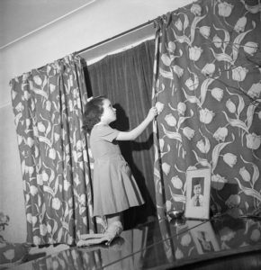 Doreen Buckner draws the curtains in her family's London home to comply with the nightly 'Blackout' [Public domain]